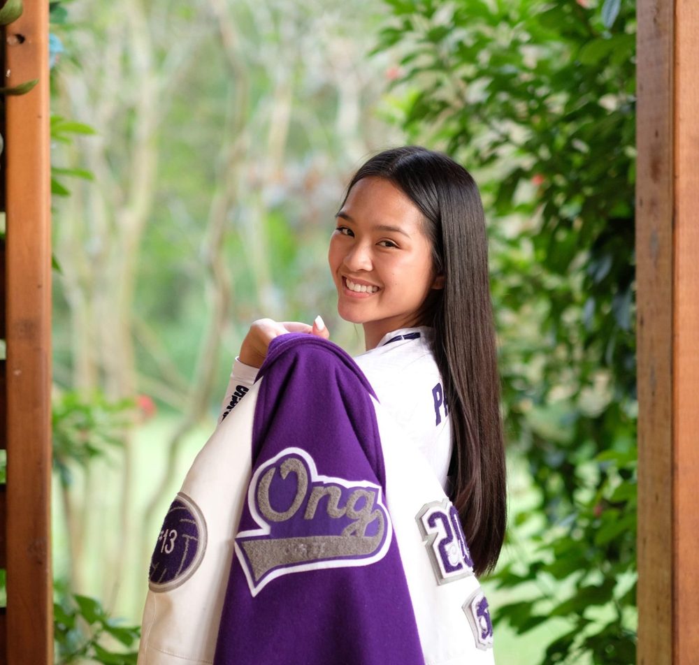 Britney smiling over her shoulder, holding her purple letter jacket with “Ong” on the back